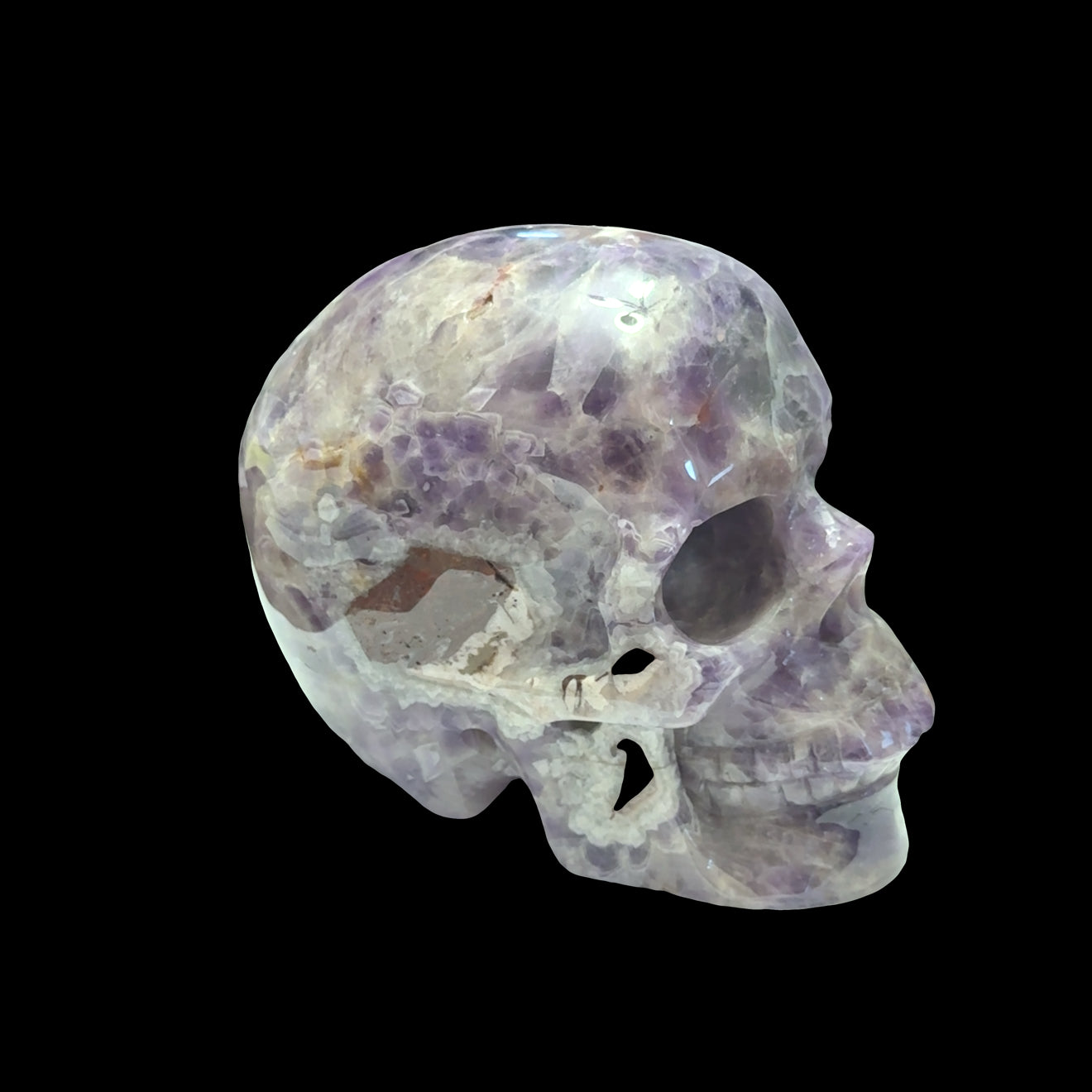 The largest of the two Trapiche Amethyst Gemstone carved skull on a black background, left side, front view. 