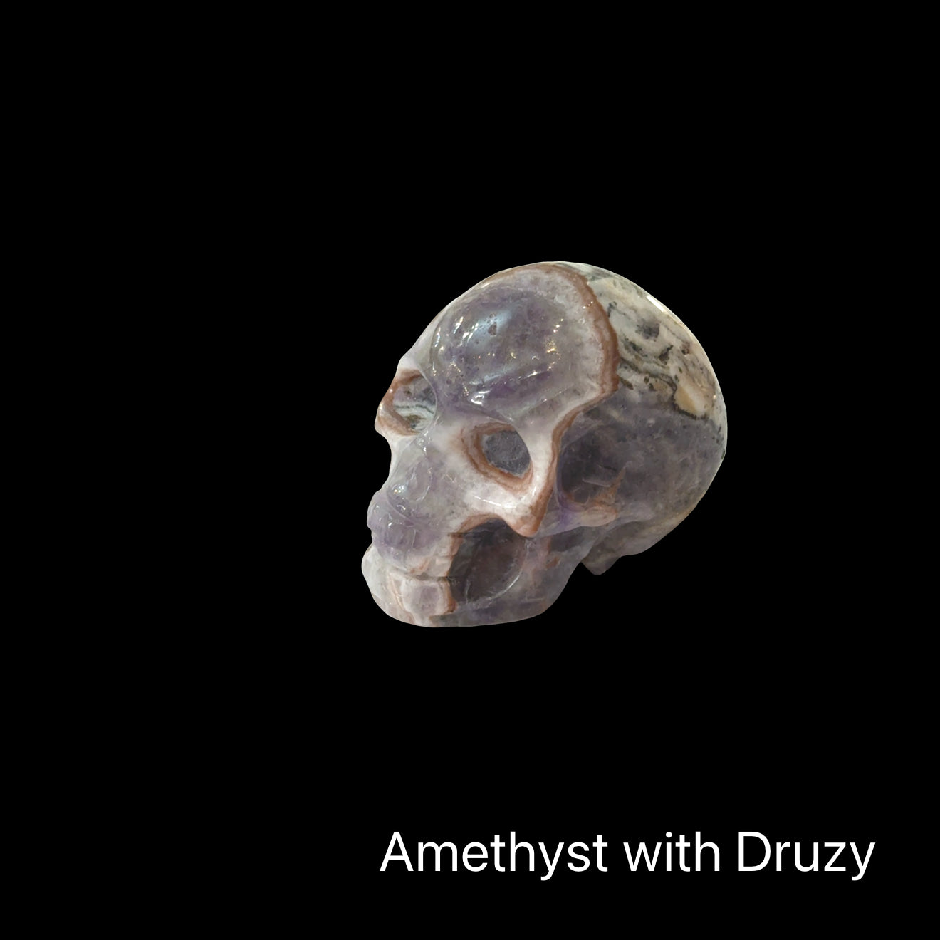 The smallest of the two Trapiche Amethyst Gemstone carved skull on a black background, left angled, front view. 