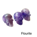 Three purple fluorite crystal skulls on a white background, front view. 