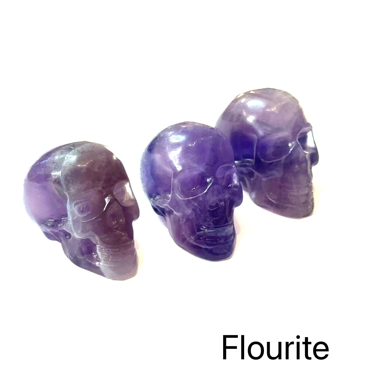 Three purple fluorite crystal skulls on a white background, front view. 