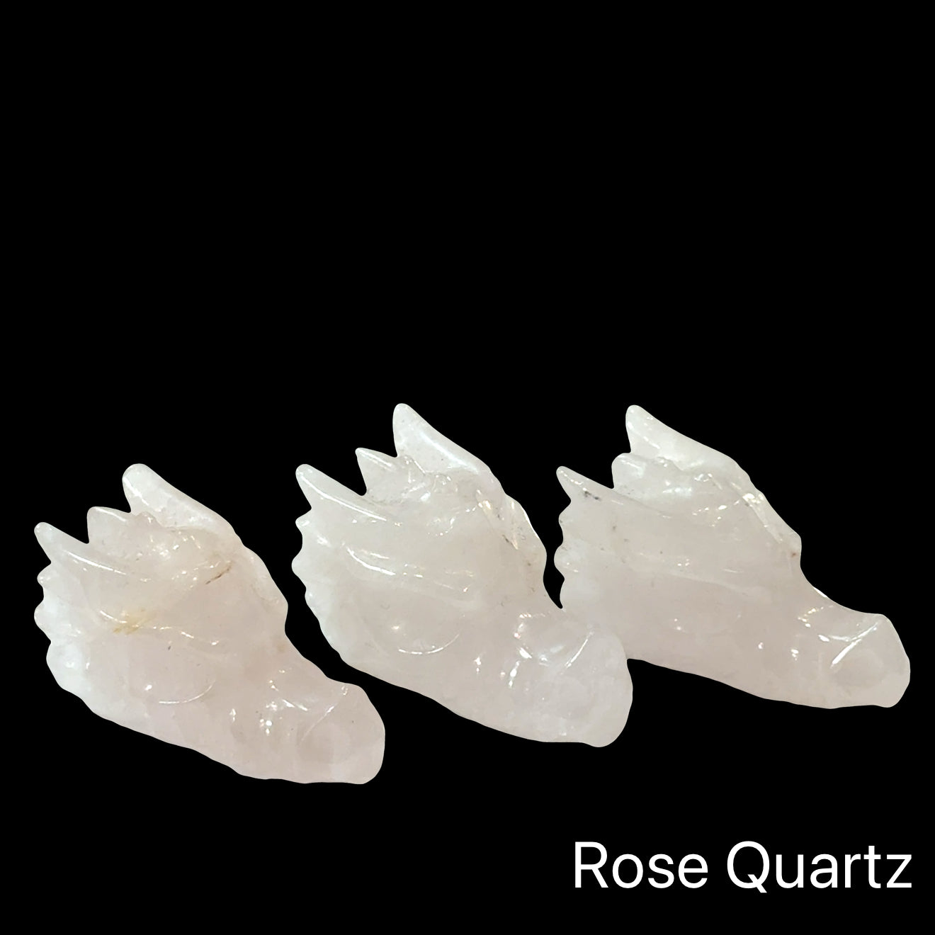 Three rose quartz crystal Dragon heads on a black background, front left angle view