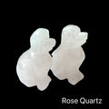 Two Rose Quartz hound Dogs gemstone carving on black background, front view.