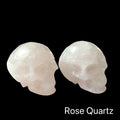 Two rose quartz gemstone skulls on a black background, in a front-right angle view. 
