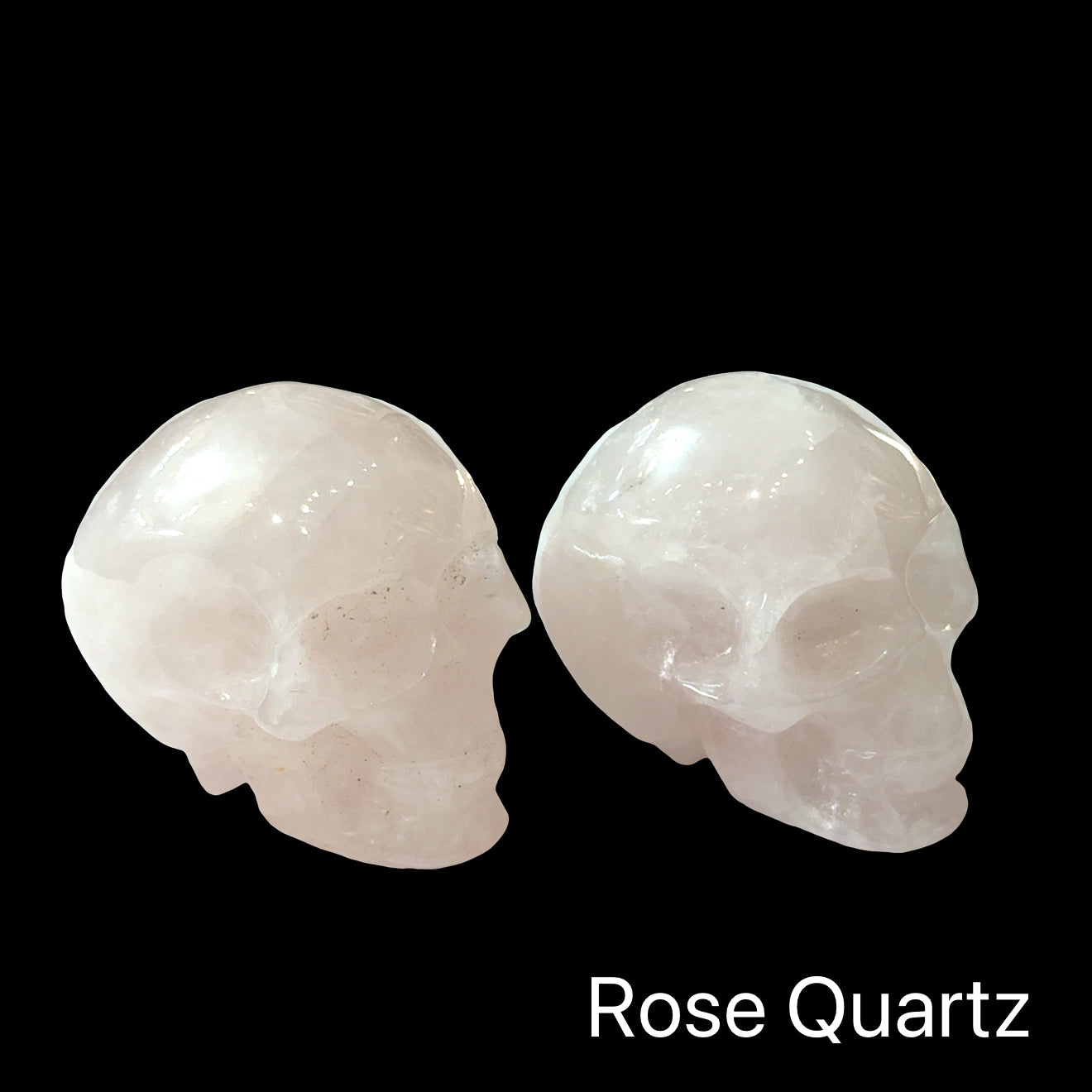 Two rose quartz gemstone skulls on a black background, in a front-right angle view. 