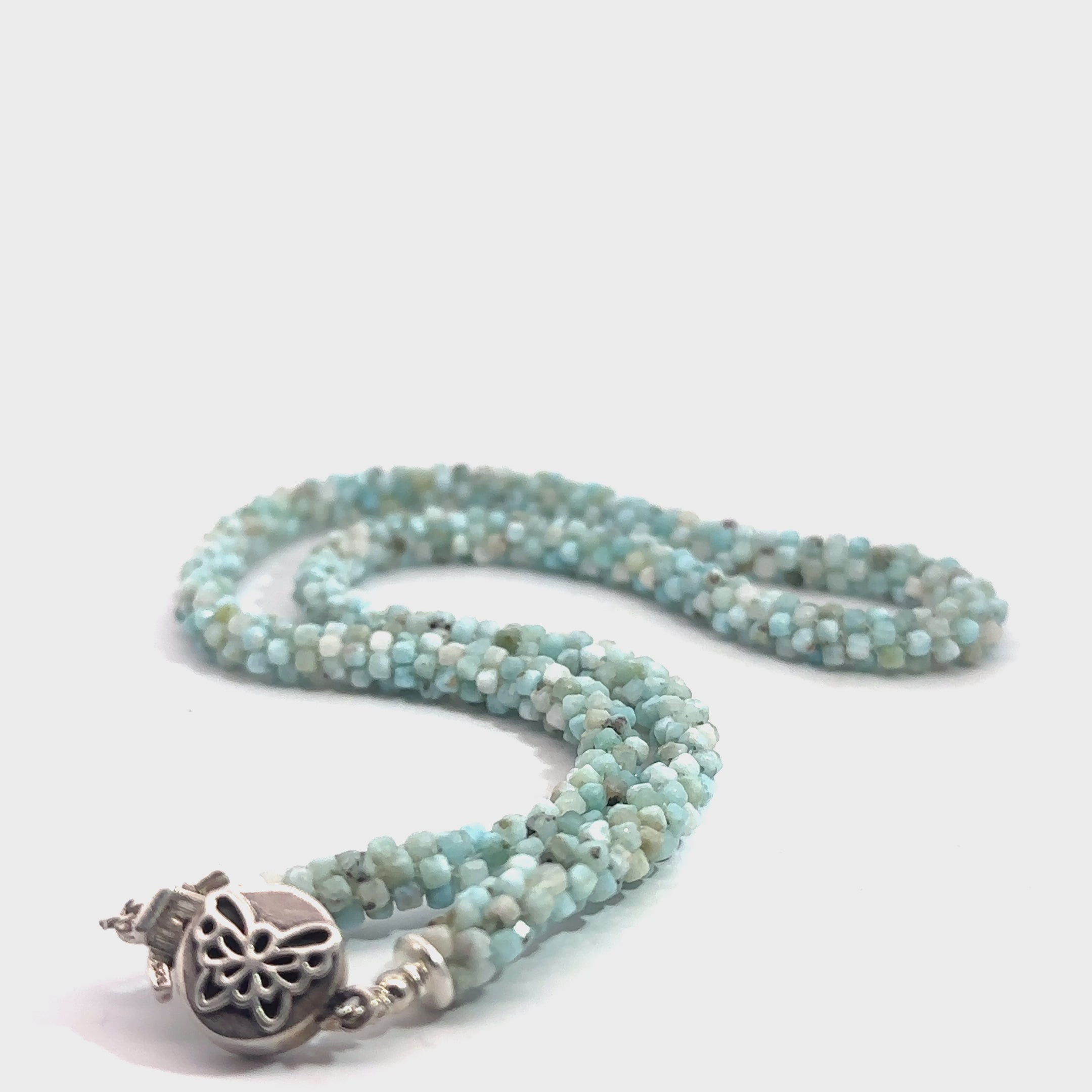 A crocheted necklace made with Larimar gemstone beads and a sterling silver butterfly box clasp on a white background, long front view. video
