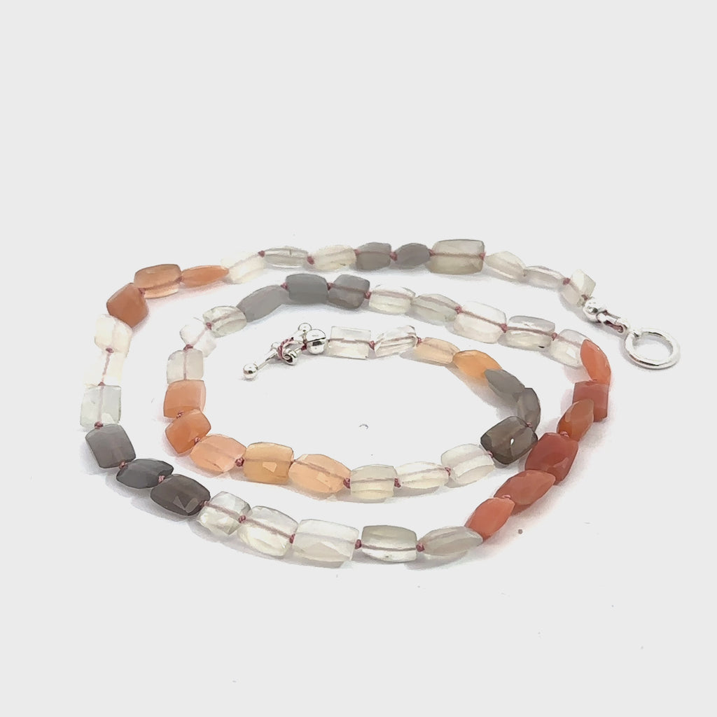 A knotted necklace made of mixed moonstone gemstones with a sterling silver toggle clasp on a white background, spiral overview. video
