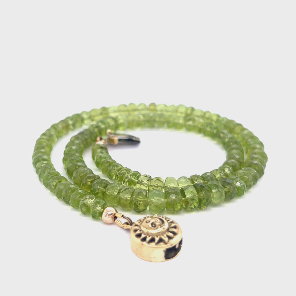 A green beaded peridot gemstone necklace with gold-filled findings and a sun and moon box clasp on a white background, spiral overview. video