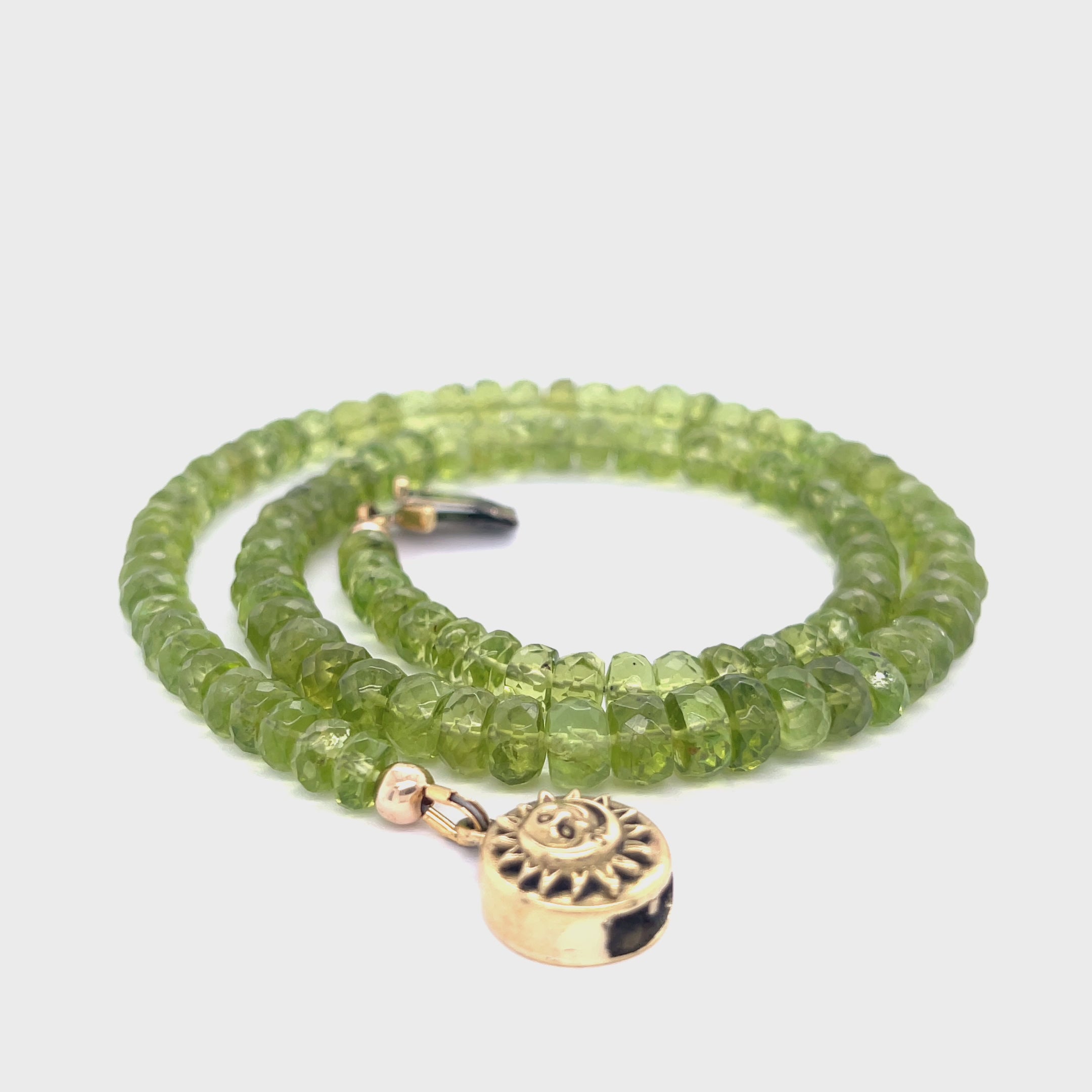 A green beaded peridot gemstone necklace with gold-filled findings and a sun and moon box clasp on a white background, spiral overview. video