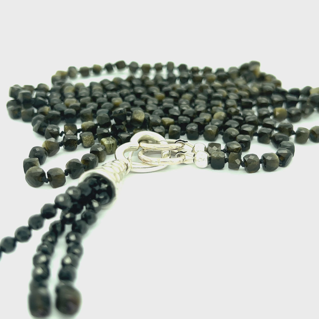 A knotted necklace made of Golden Sheen Obsidian gemstones with a tassel, featuring silver accents. On a white background, a long, center view overview.  video