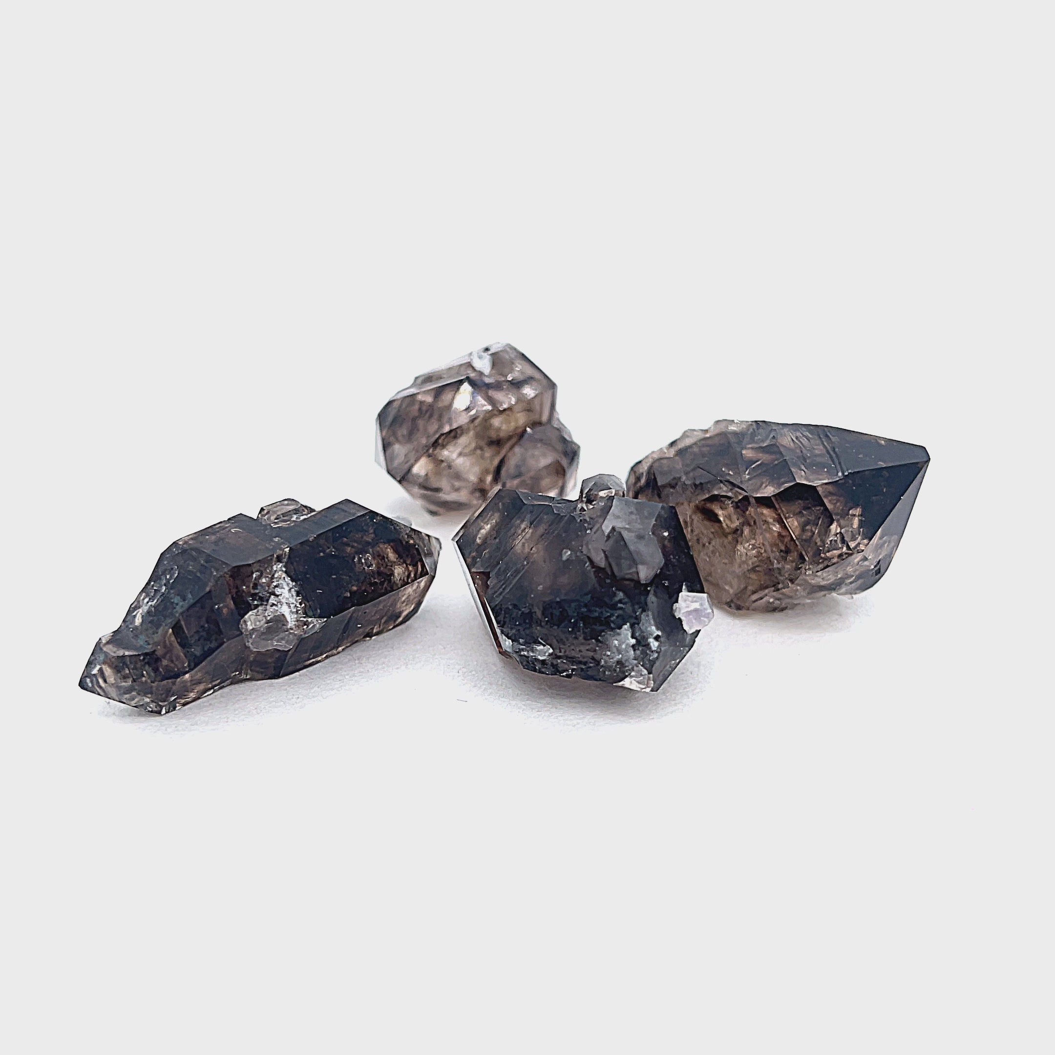 A collection of raw Smokey Quartz gemstones with a dark, smoky appearance, displayed on a white background in a front view. video