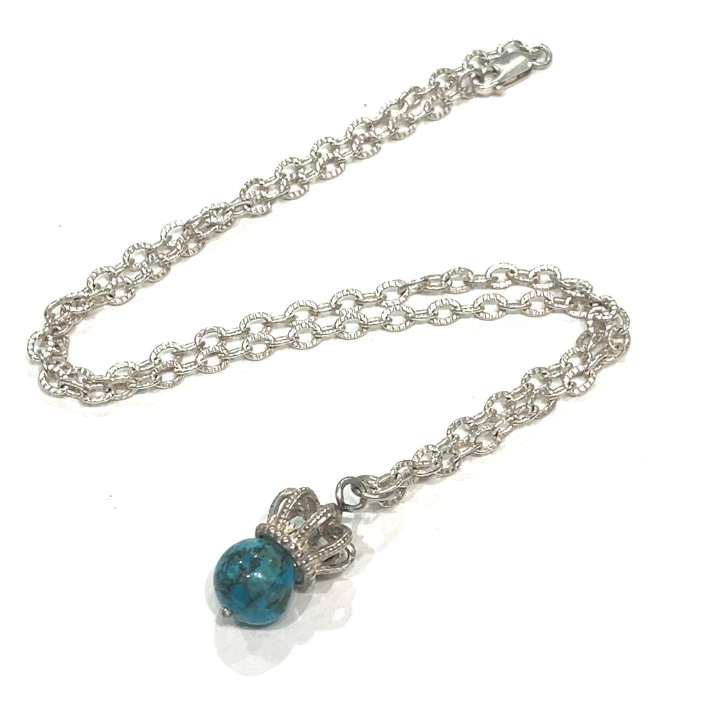 A Sterling Silver Crown Pendant with turquois  gemstone on a white background, laying on a diagonal center view.   