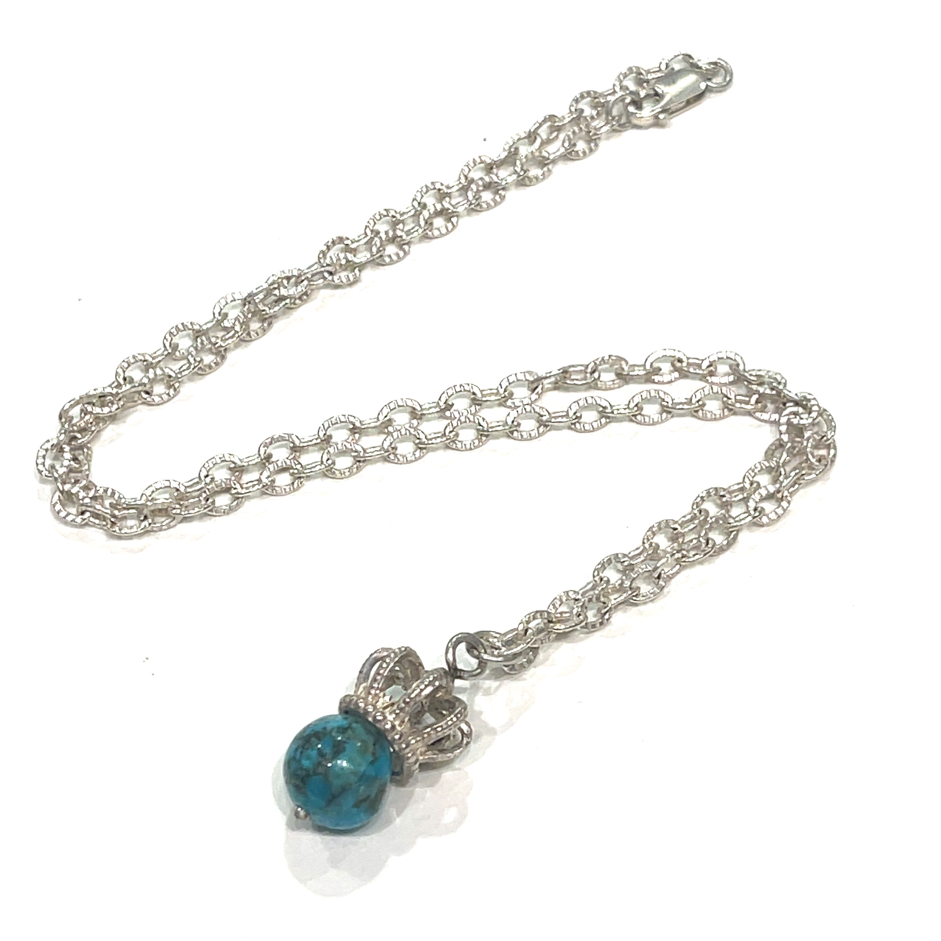 A Sterling Silver Crown Pendant with turquois  gemstone on a white background, laying on a diagonal center view.   