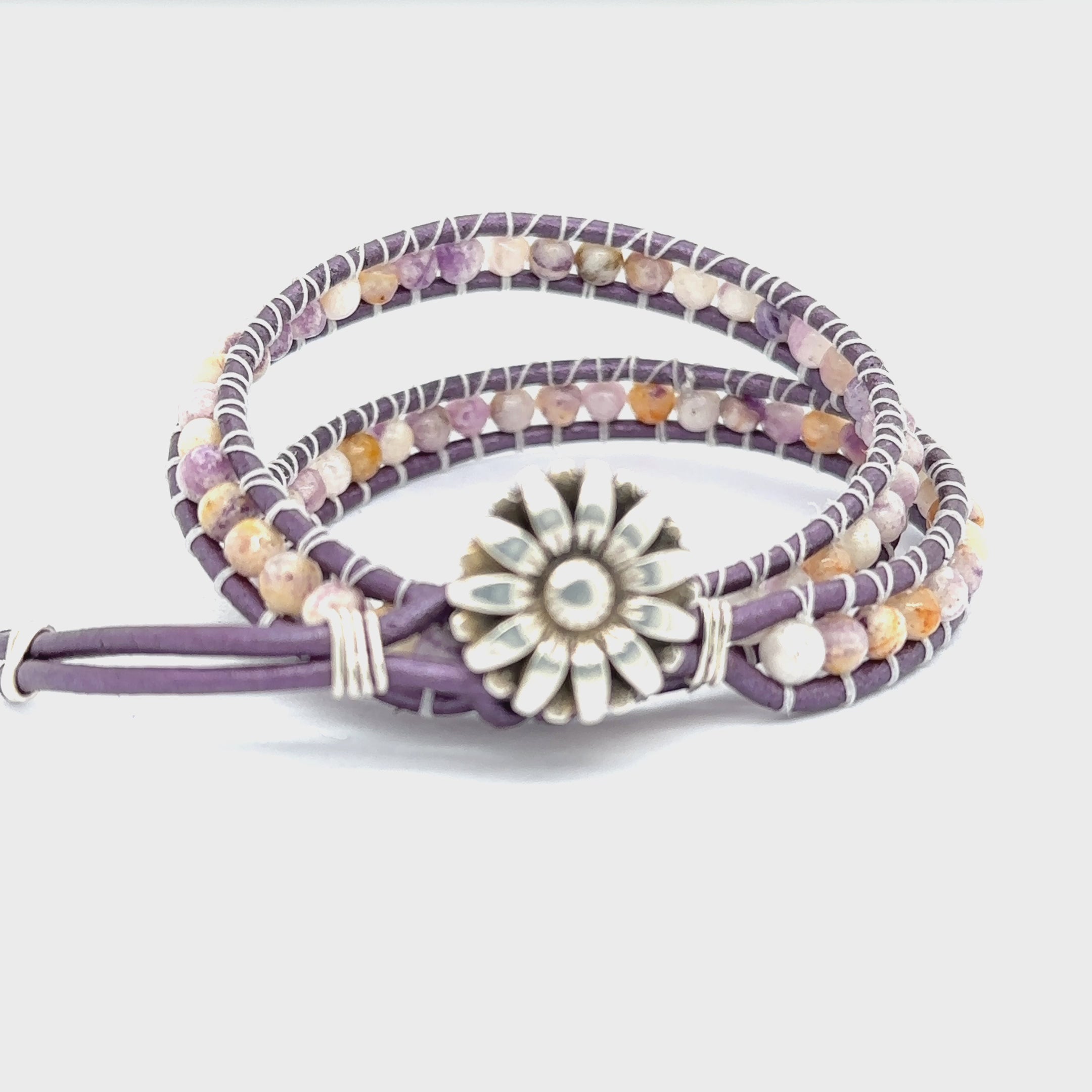 A double leather wrap bracelet made out of purple flower agate, featuring a floral button, and measuring 15.5 inches in length. On a white background button view video.