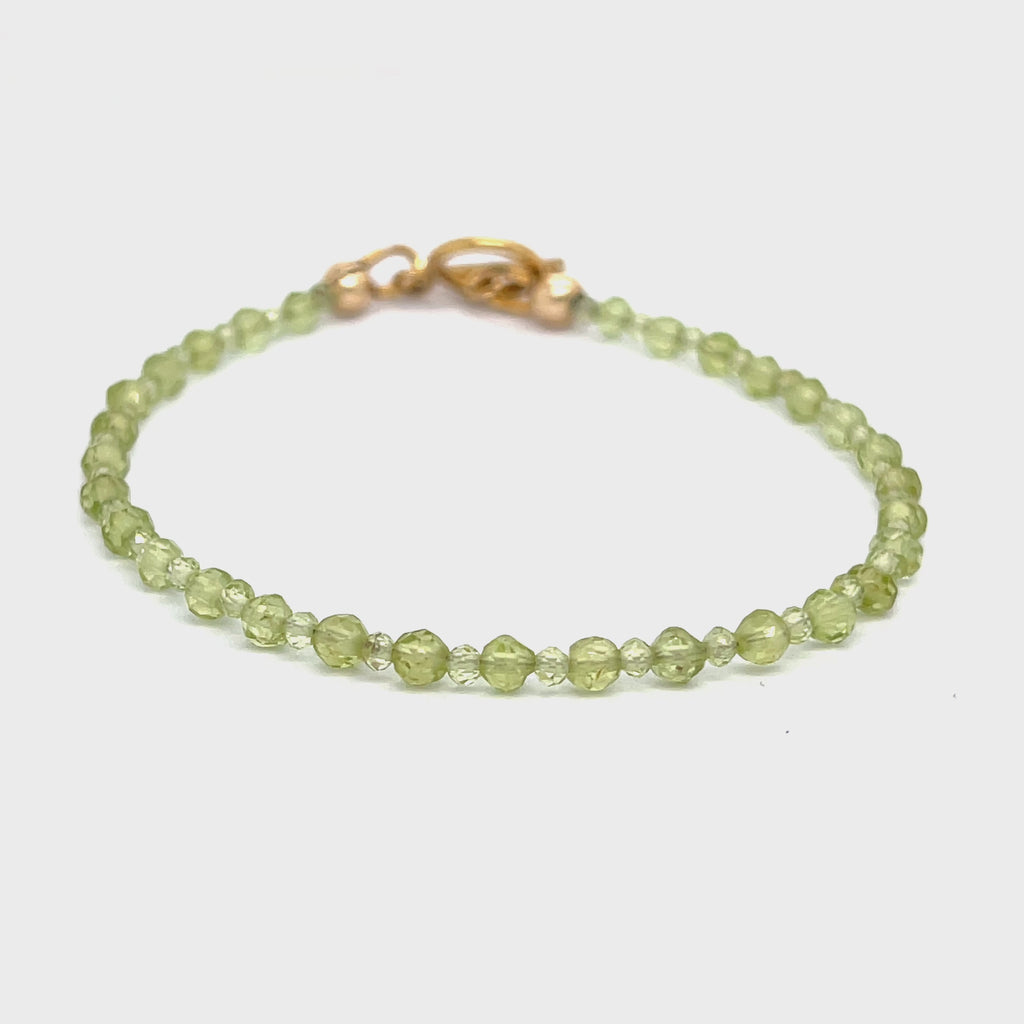 A peridot gemstone 2-3mm faceted round with a gold filled toggle on a white background front overview. video