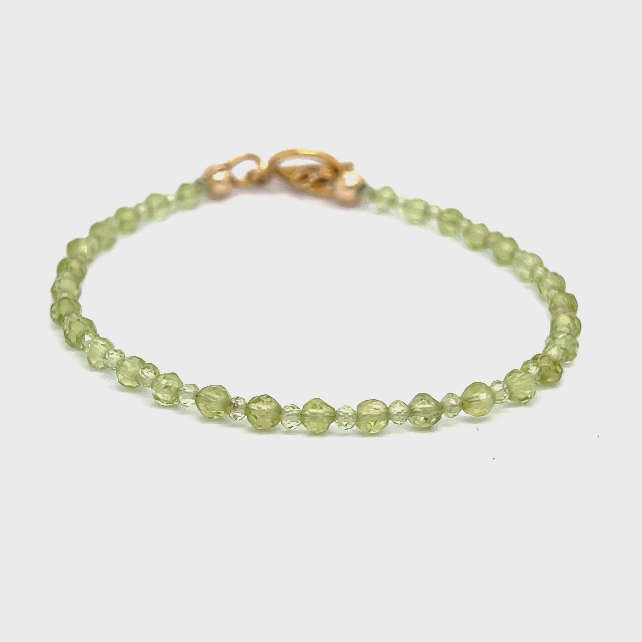 A peridot gemstone 2-3mm faceted round with a gold filled toggle on a white background front overview. video