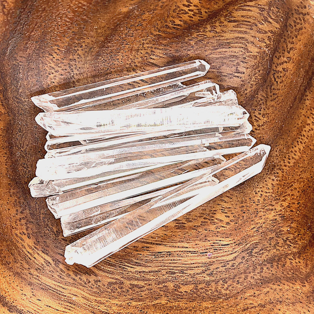 A hand holding several clear quartz gemstone wands with a wood background, front view video