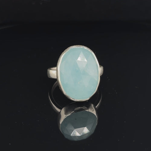 Aquamarine gemstone ring with a bezel-set design, worn on a model's finger, with a matching nail polish in the background front overview. video