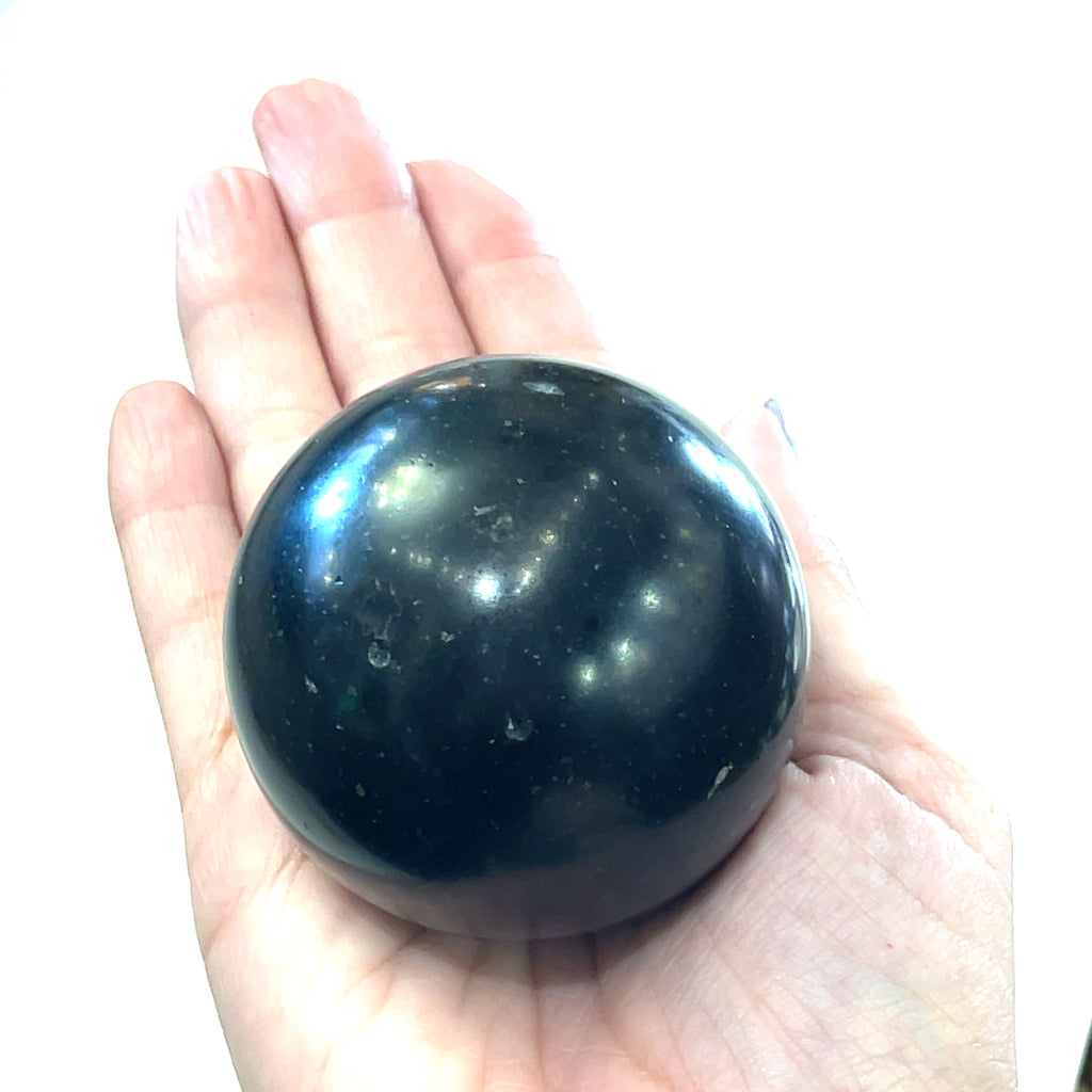 A  Black Tourmaline Sphere in a models palm  used for energy grounding and meditation on a white background front view. 