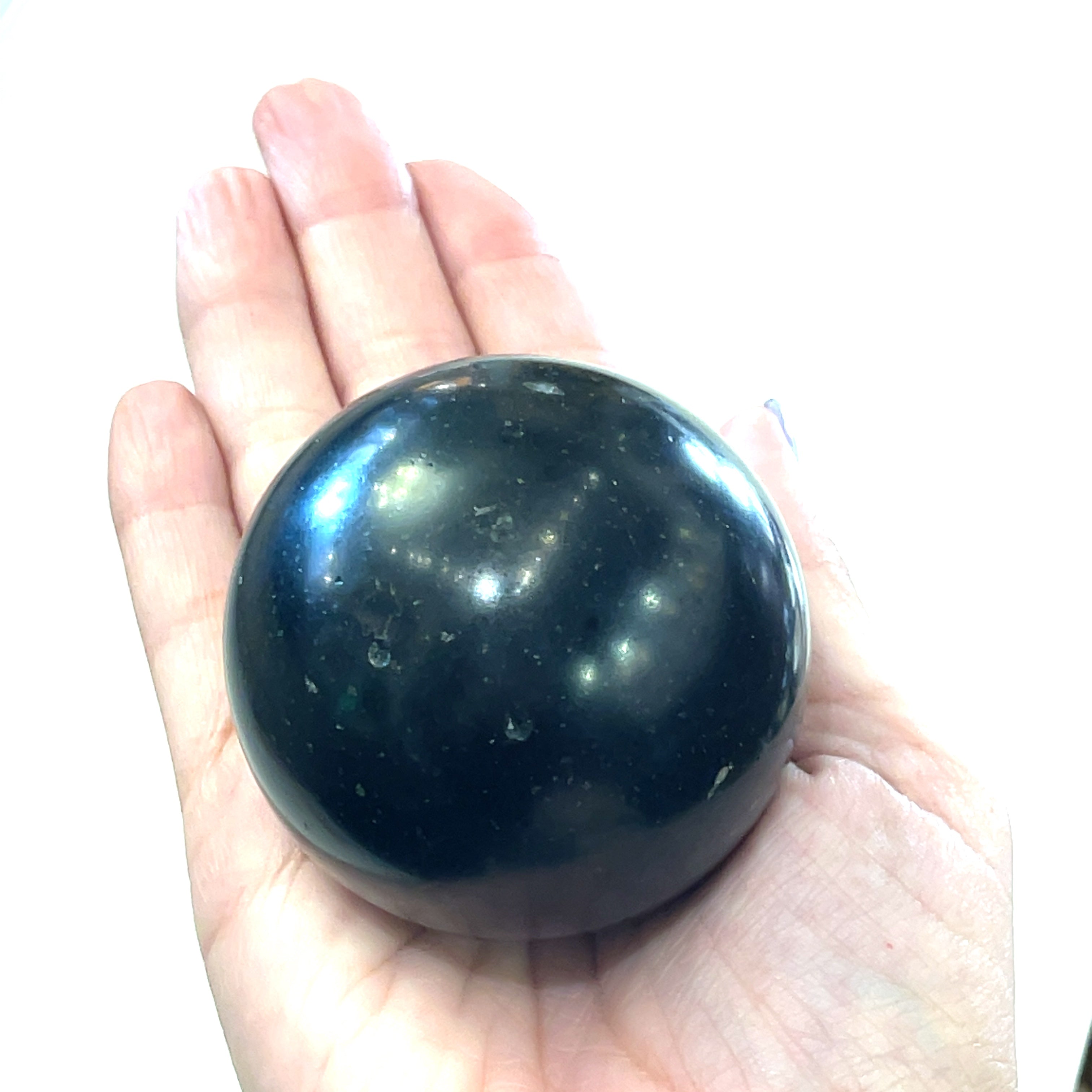 A  Black Tourmaline Sphere in a models palm  used for energy grounding and meditation on a white background front view. 