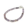 A Close-up of the Super Seven gemstone bracelet with 6mm faceted beads and a sterling silver toggle clasp. On a white background, front left angle view. 