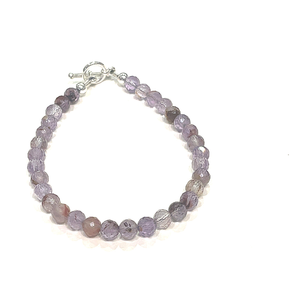 A Close-up of the Super Seven gemstone bracelet with 6mm faceted beads and a sterling silver toggle clasp. On a white background, front view. 