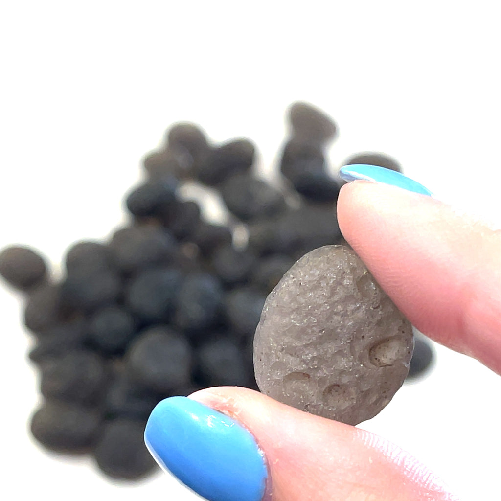 A Close-up view of Colombianite showing natural volcanic texture and obsidian luster in a models fingertips. Front view. 