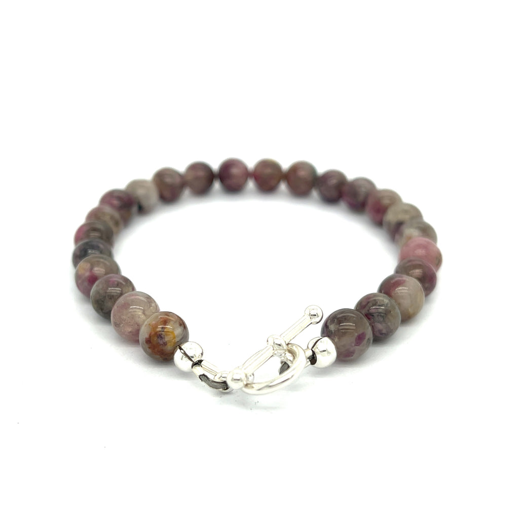 A Eudialyte gemstone beaded bracelet with a sterling silver toggle on a white background back center overview.