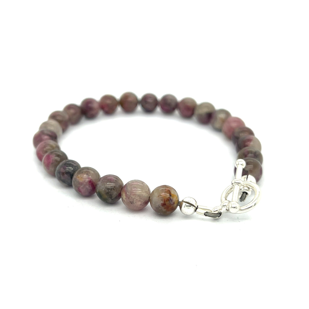 A Eudialyte gemstone beaded bracelet with a sterling silver toggle on a white background back right angle overview.