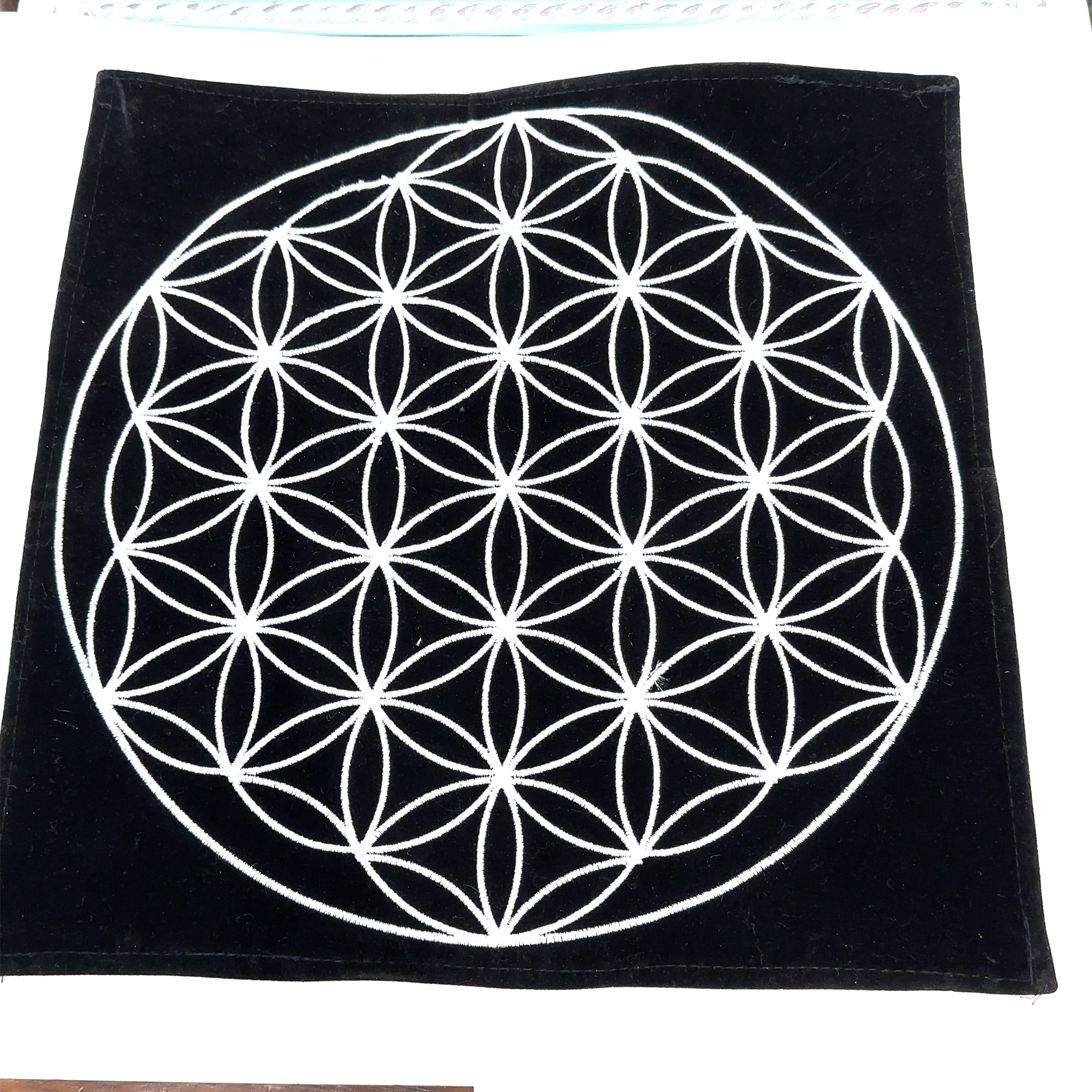 A Flower of Life 12x12 black velvet mat with white embroidery on a white background overview.  