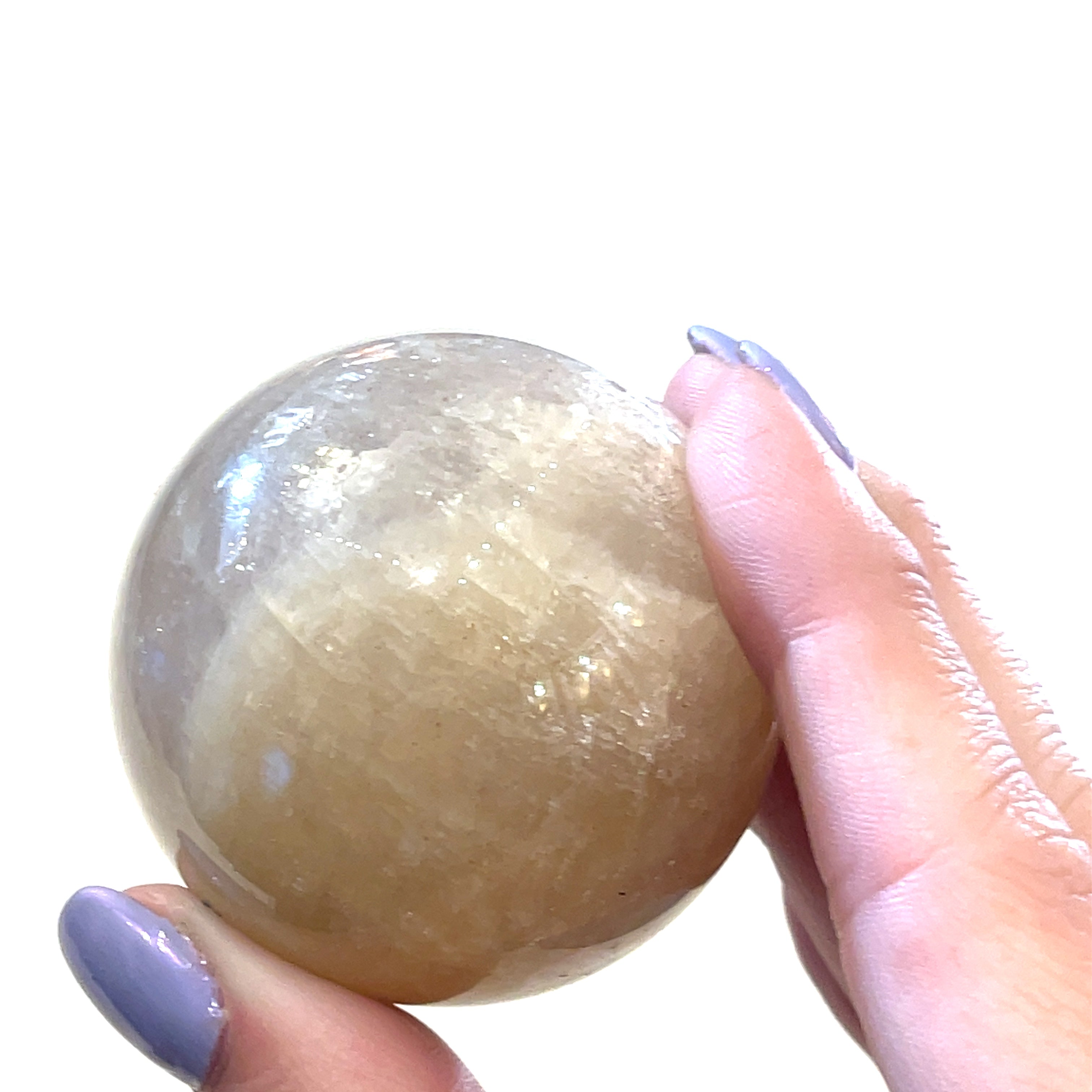 A Grey Moonstone Sphere for meditation, balance, and chakra work in a models hand on a white background a close up view. 
