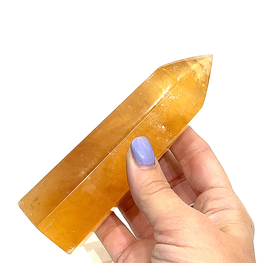 A Honey Calcite gemstone towers displayed in a models hand on a white background, front view.