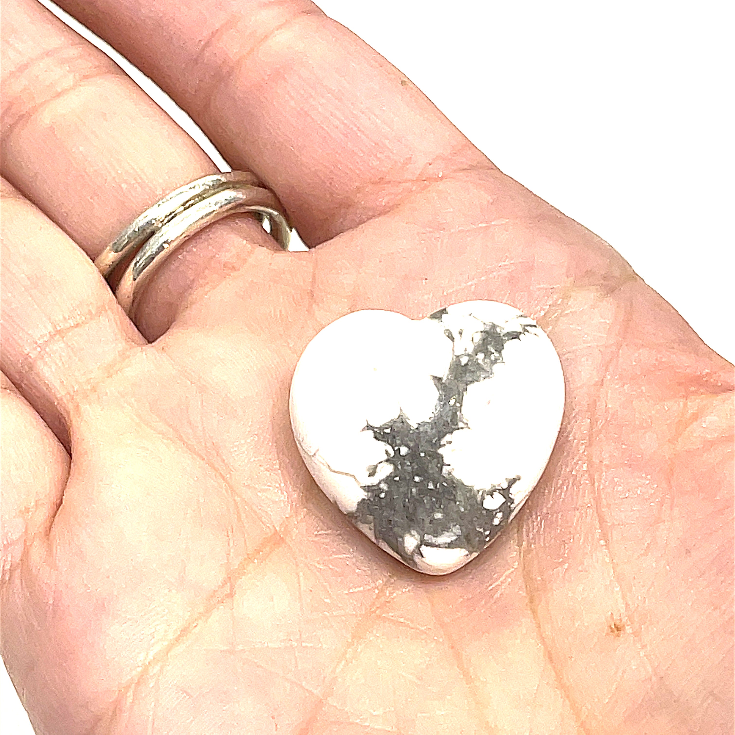 A Howlite gemstone with a white and gray marbled pattern displayed on a models palm on a white background, front view. 