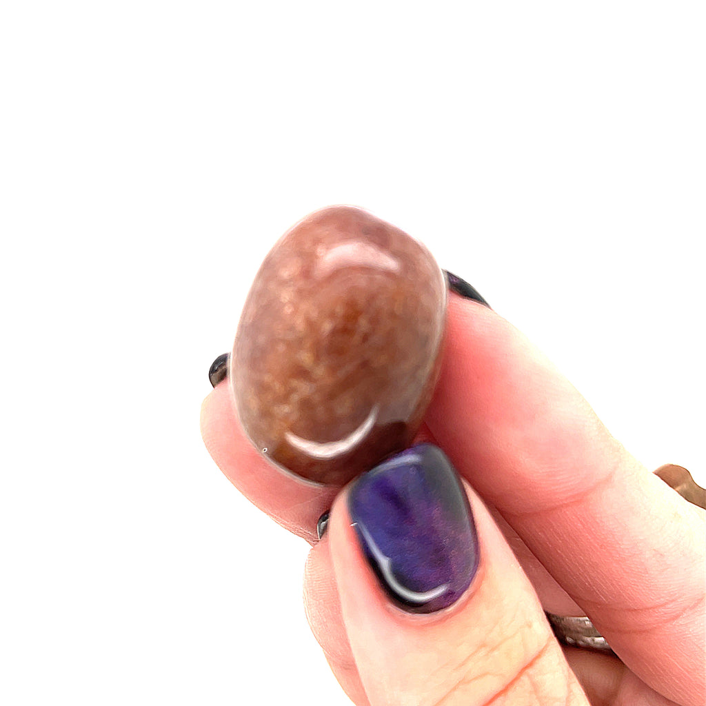 A Muscovite tumbled gemstones on a white background, in a models finger tips. front overview.
