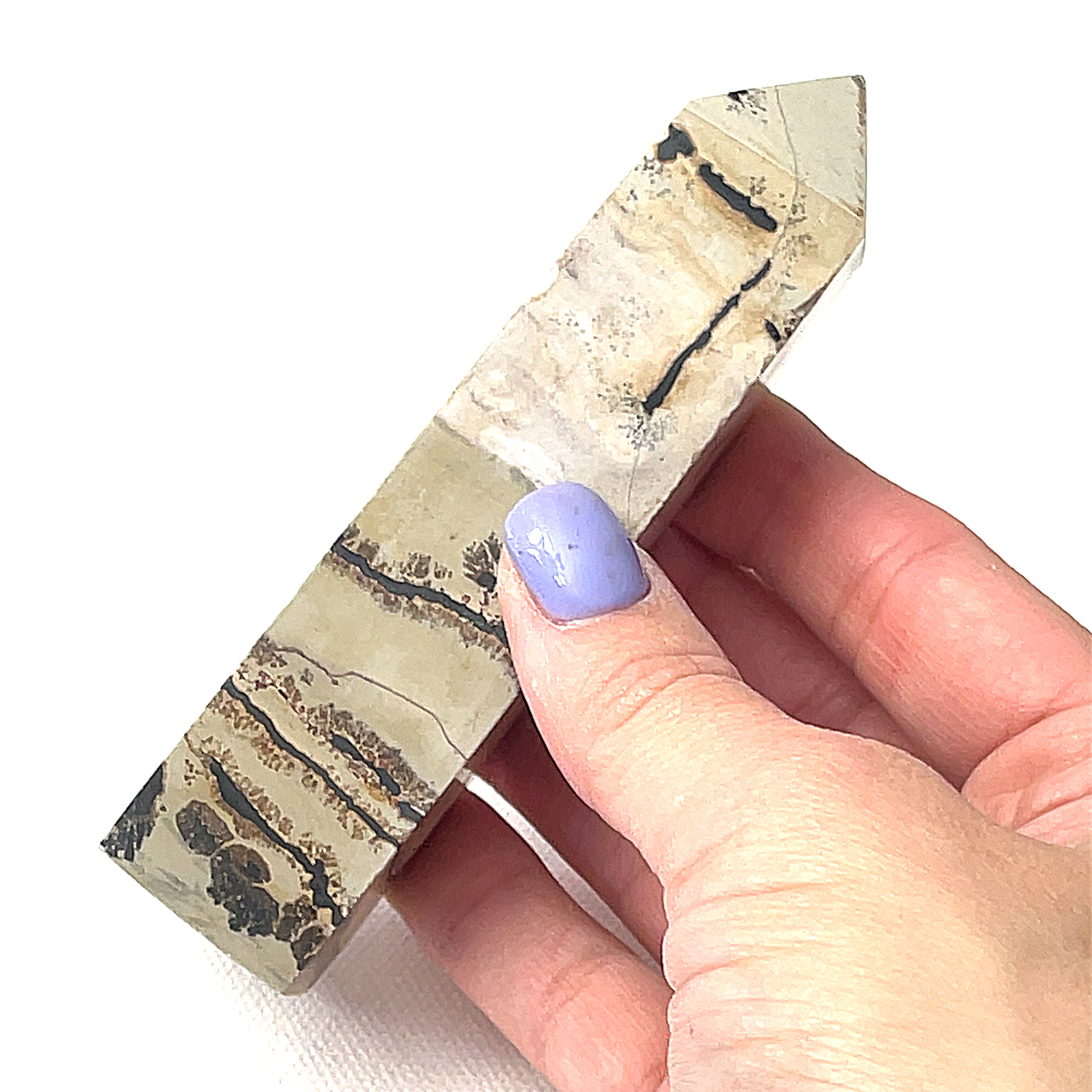 A Picture Jasper gemstone tower in a models finger tips, on a white background, front view. 