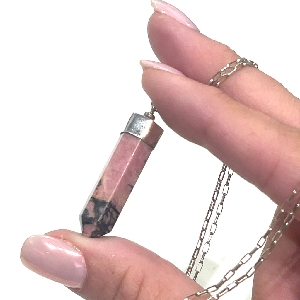 A Rhodonite gemstone pendant on a sterling silver chain. On a white background and in a models finger tips for a close up overview. 