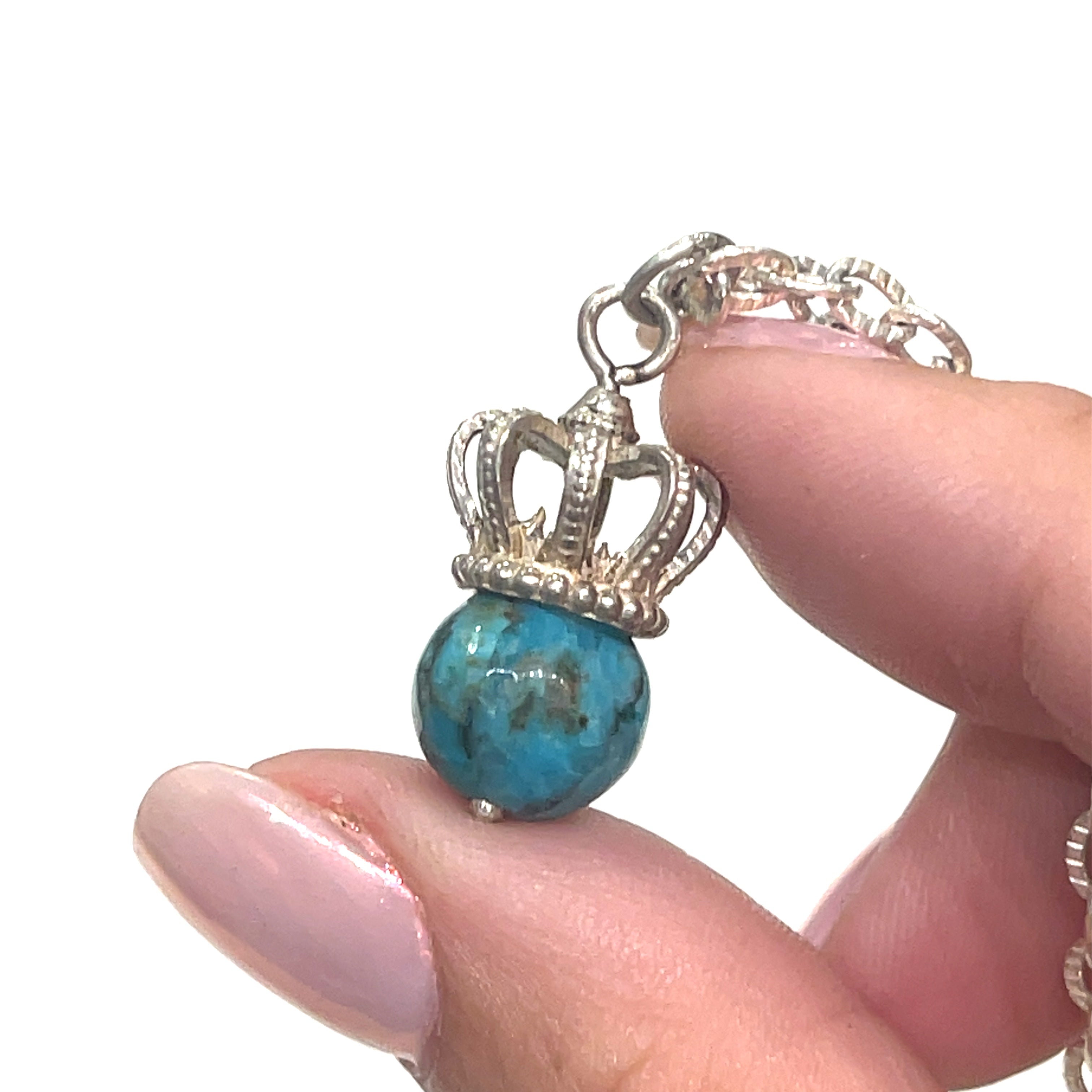 A Sterling Silver Crown Pendant with turquois  gemstone on a white background, in a models finger tips.  