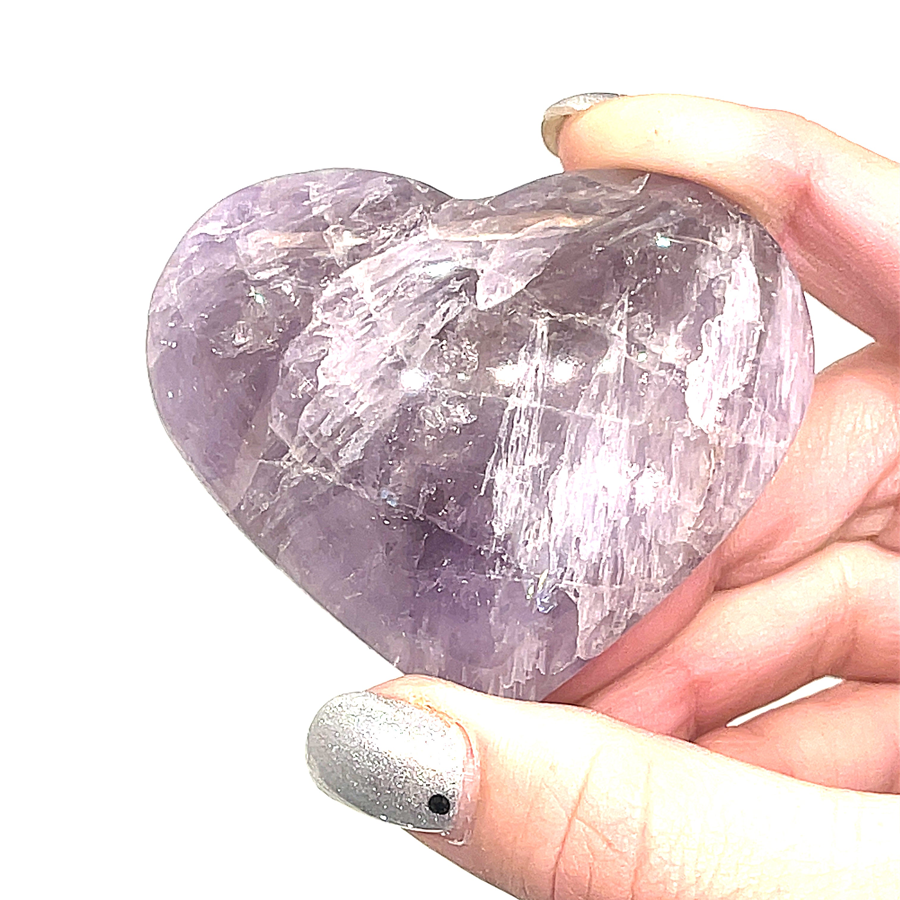 A Super Seven gemstone heart carving, held by a model for a close-up, front view on a white background.