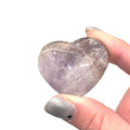 A Super Seven gemstone heart carving, in a models finger tips for a close-up, overview on a white background.
