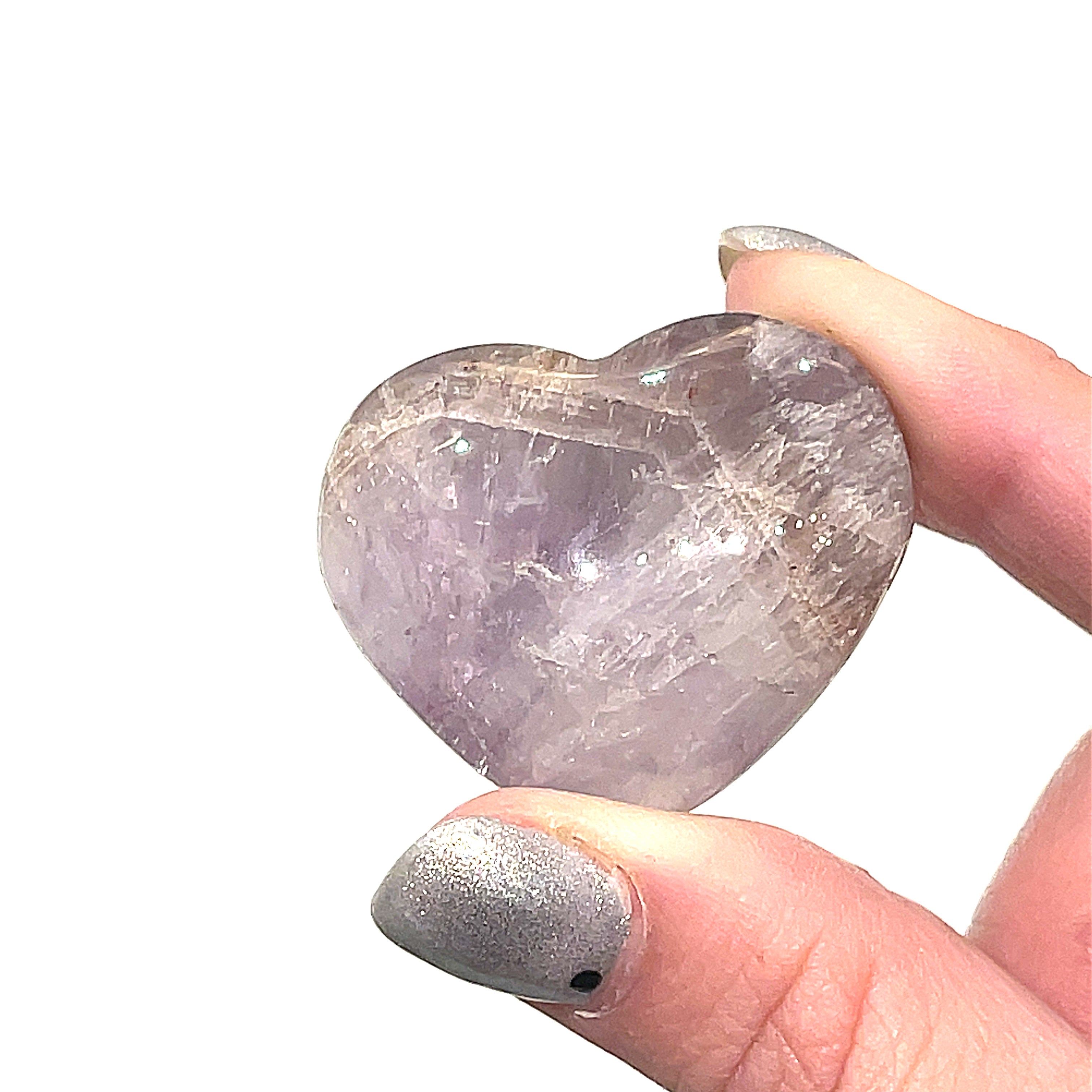 A Super Seven gemstone heart carving, in a models finger tips for a close-up, overview on a white background.