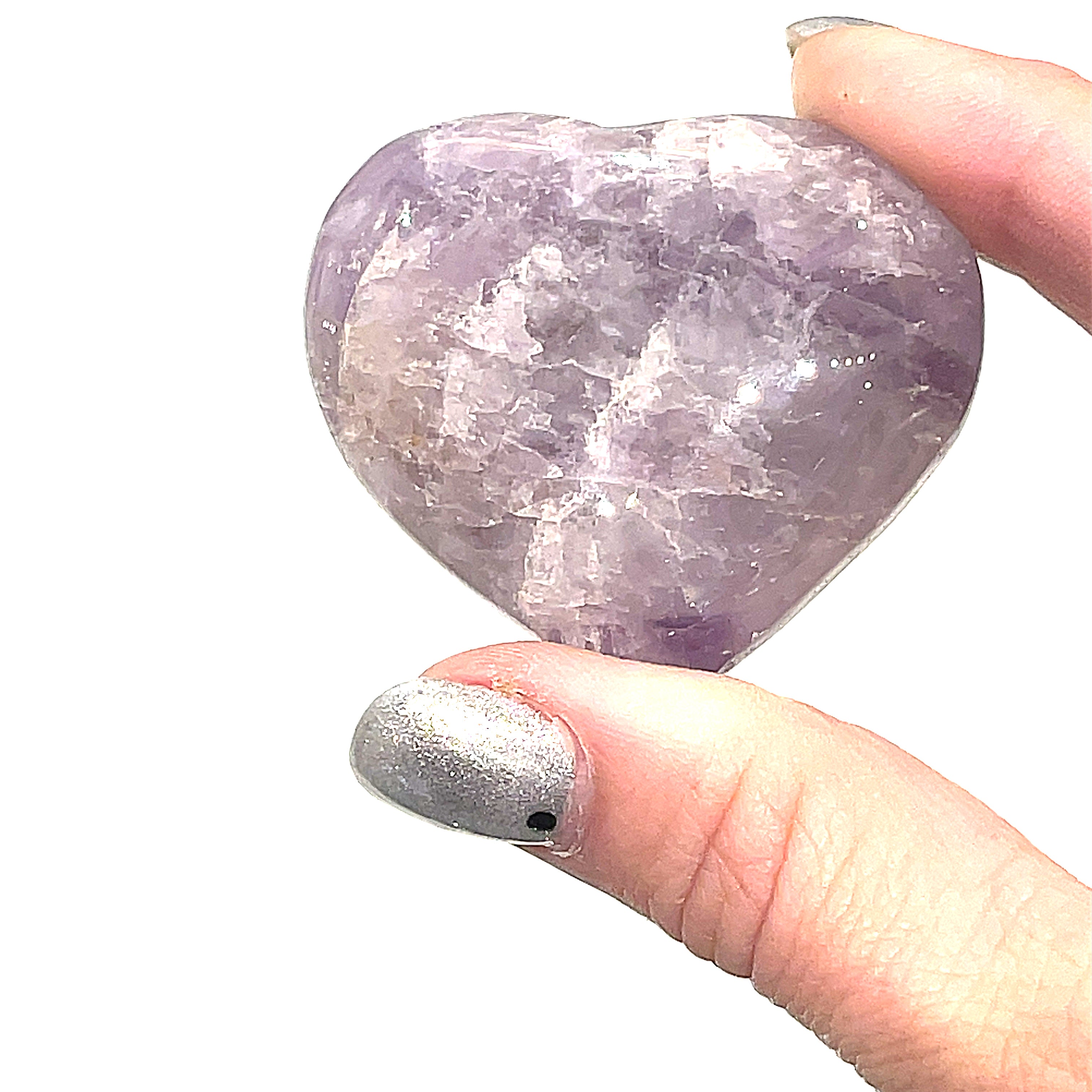 A Super Seven gemstone heart carving, in held in a models hand for a close-up, overview on a white background.