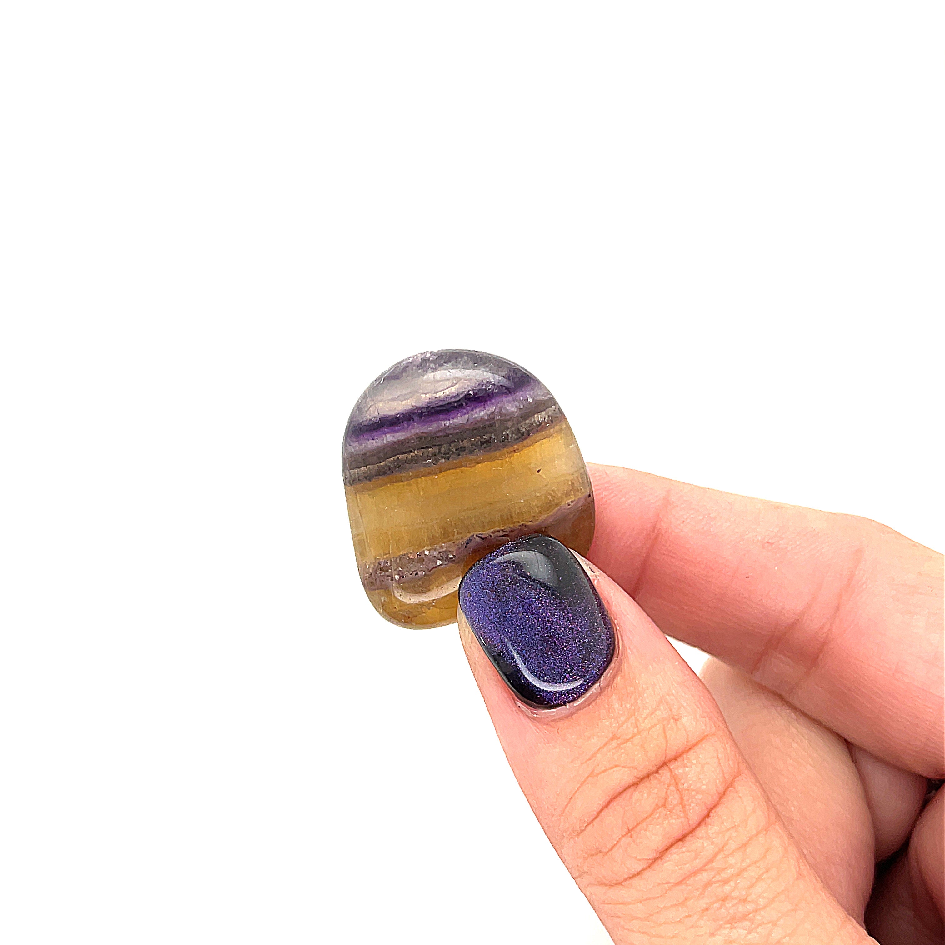 A Yellow Fluorite tumbled gemstone displayed in a models finger tips, on a white surface, front overview. 