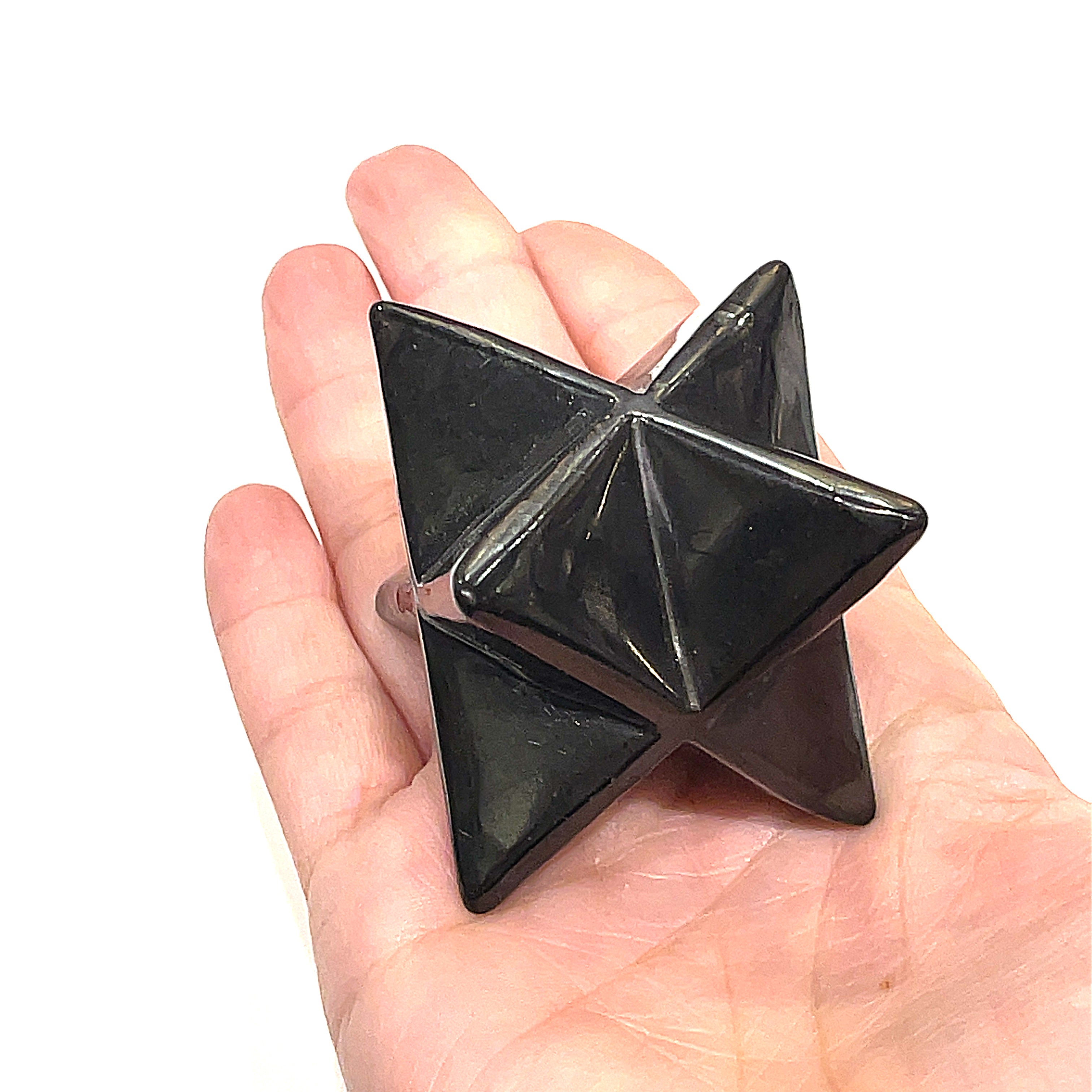 A black Shungite gemstone merkaba carvings displayed on a models hand and against a white background, front overview. 