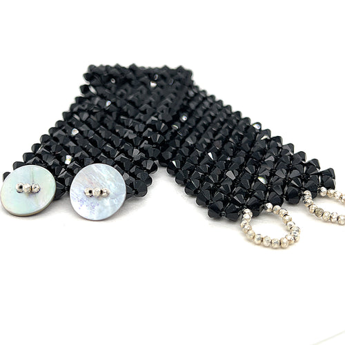 A black colored Swarovski crystal cuff bracelet with abalone shell and silver-coated pyrite buttons at the center front view on a white background.