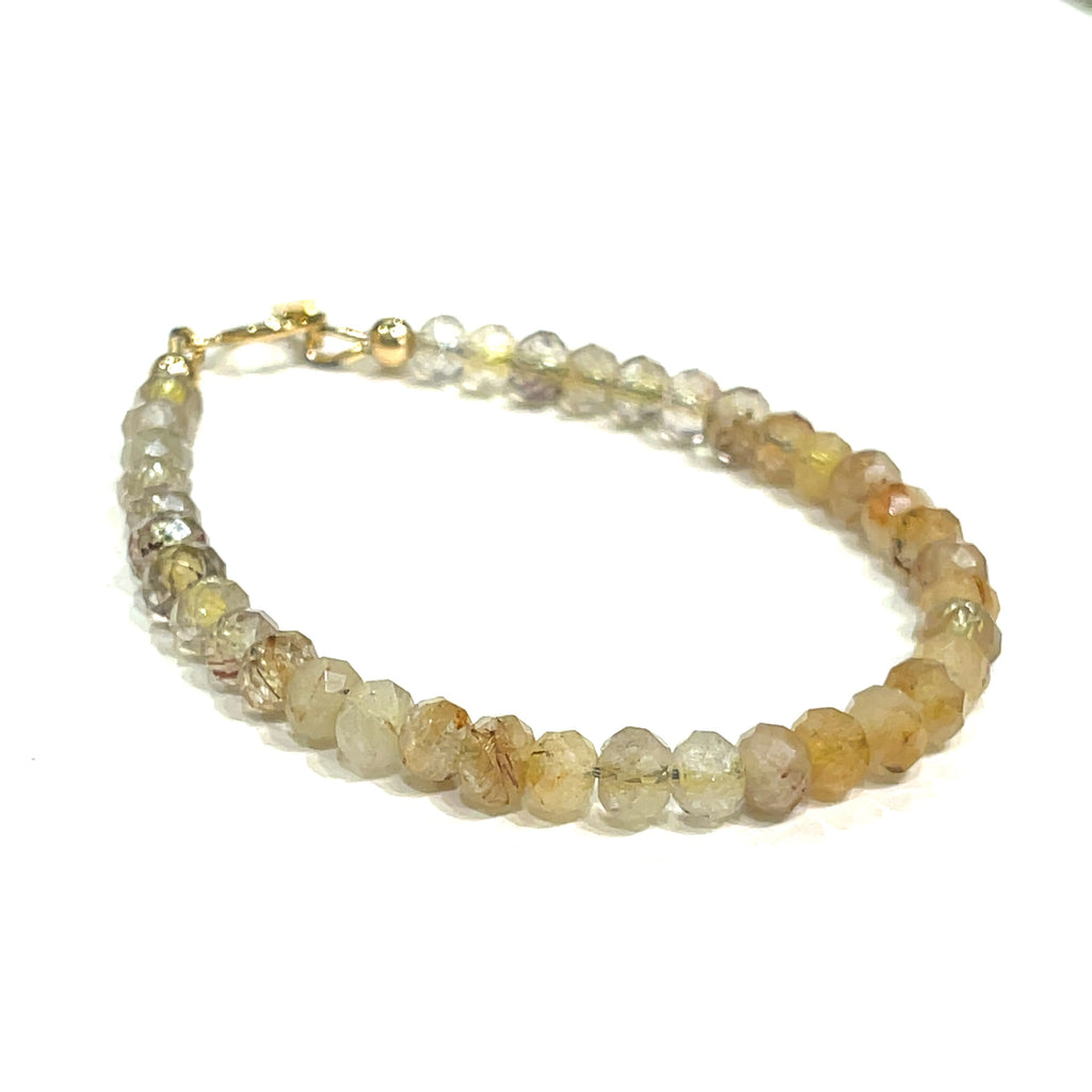 A bracelet made of faceted roundel beads of Golden Rutilated Quartz, with a gold-filled toggle closure on a white background, front, and a slight right-angle front overview. 