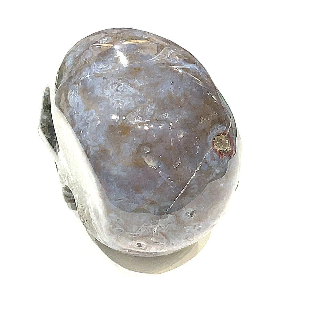 A carved gemstone skull, predominantly white in color with green accents, showcasing realistic facial features on a white background, back side view in a models hand. 