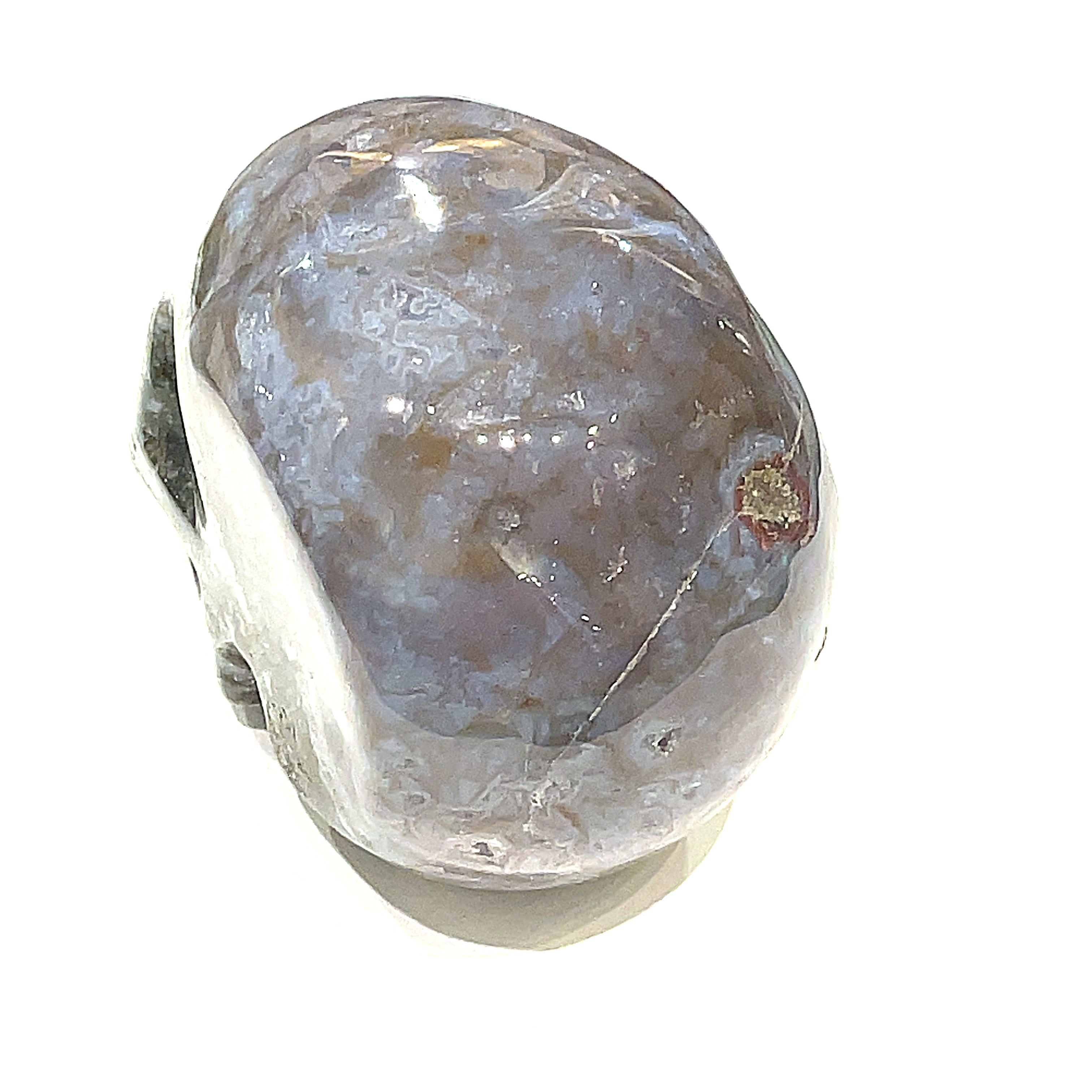 A carved gemstone skull, predominantly white in color with green accents, showcasing realistic facial features on a white background, back side view in a models hand. 