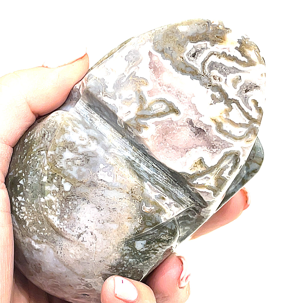 A carved gemstone skull, predominantly white in color with green accents, showcasing realistic facial features on a white background, bottom view in a models hand. 