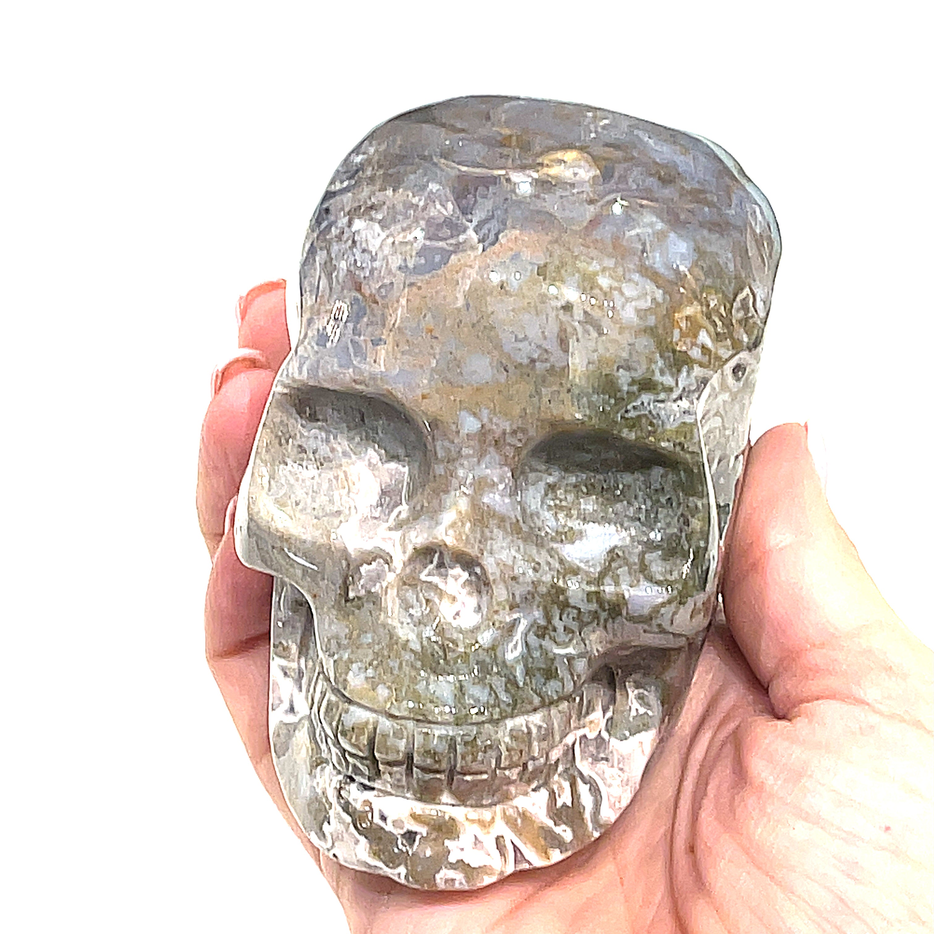 A carved gemstone skull, predominantly white in color with green accents, showcasing realistic facial features on a white background, front angle view in a models hand. 