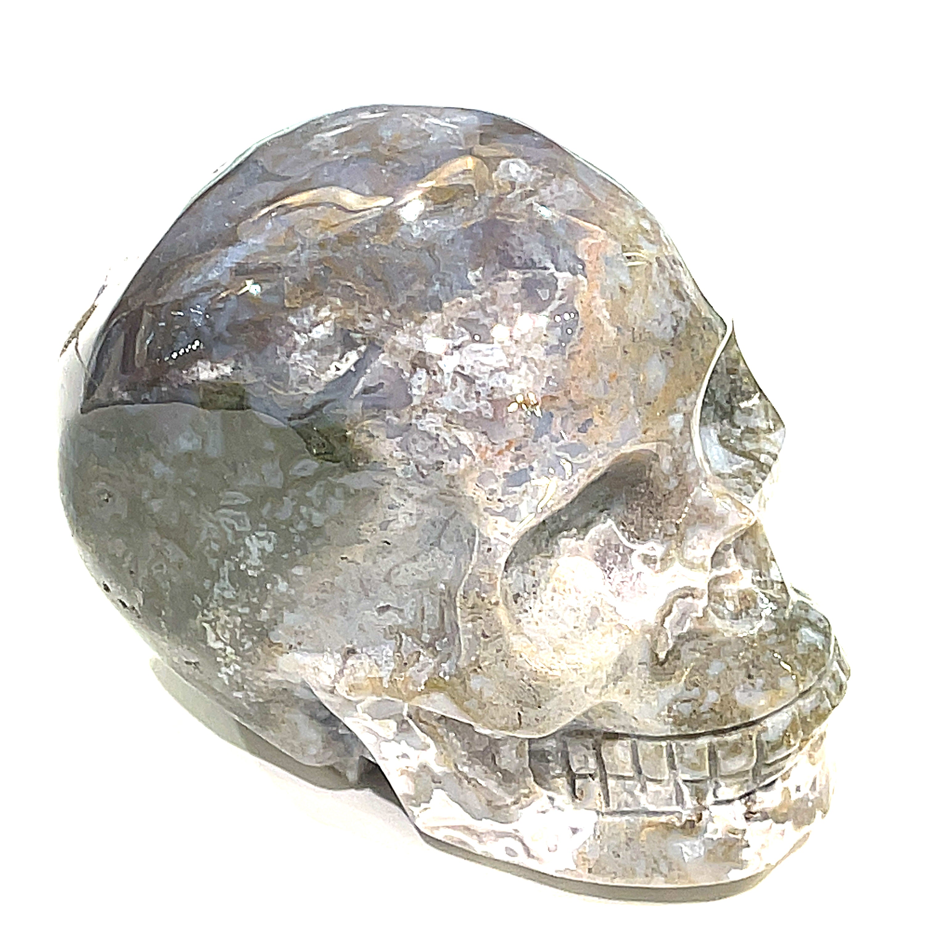 A carved gemstone skull, predominantly white in color with green accents, showcasing realistic facial features on a white background, left side front angle view. 