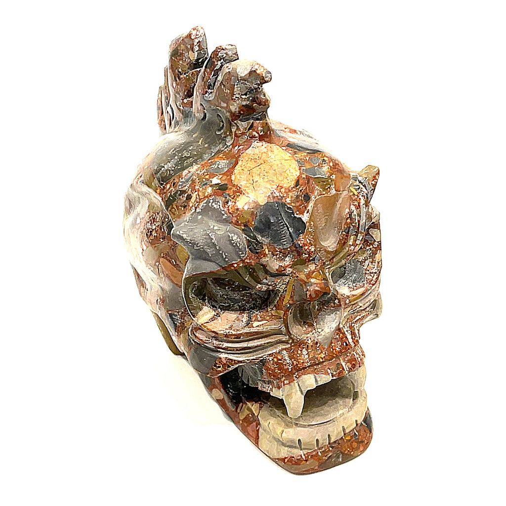 A carved jasper skull alter stones with a dragon mohawk design on a white background,  left-angle front view. 